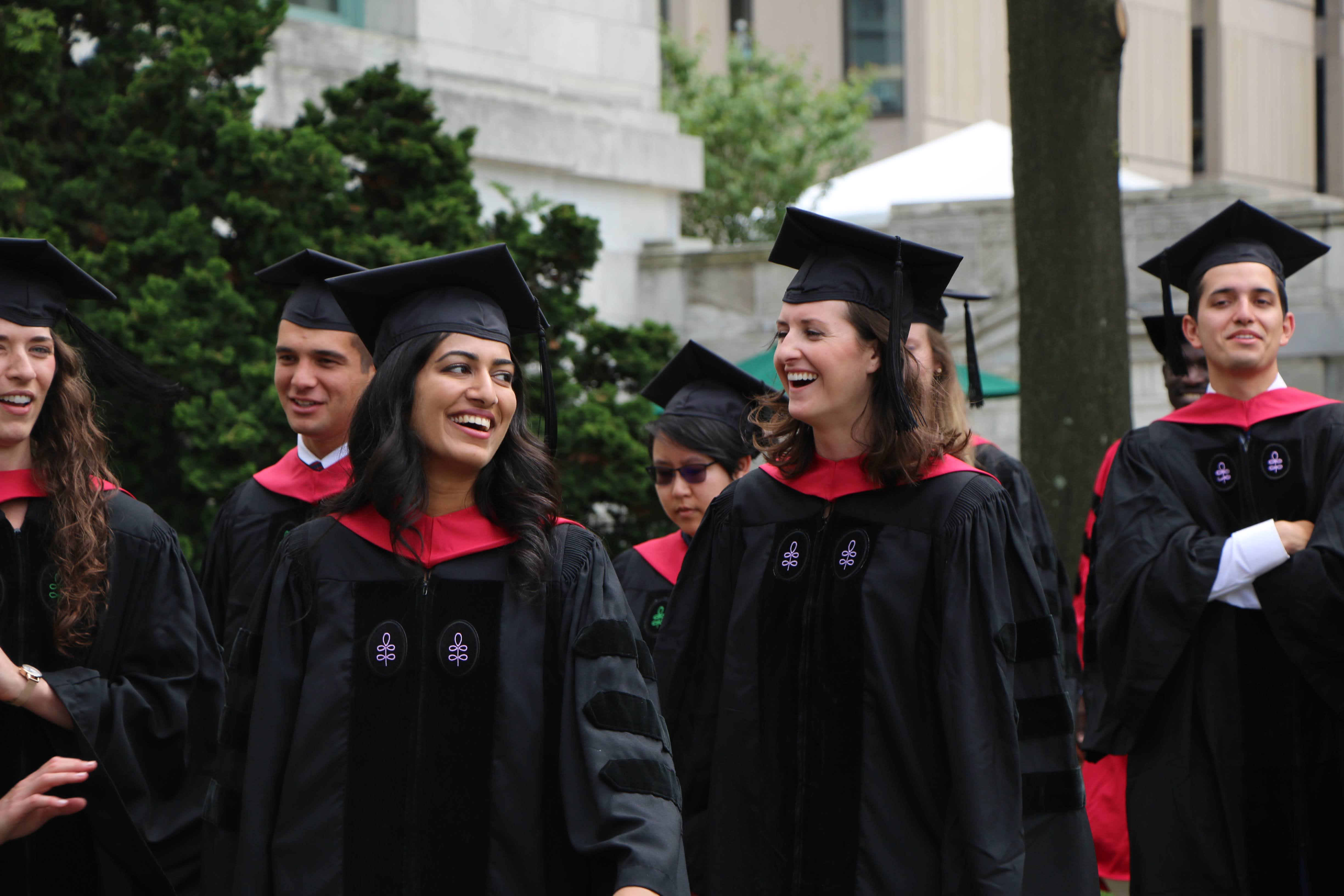Two students walking outside wearing regalia
