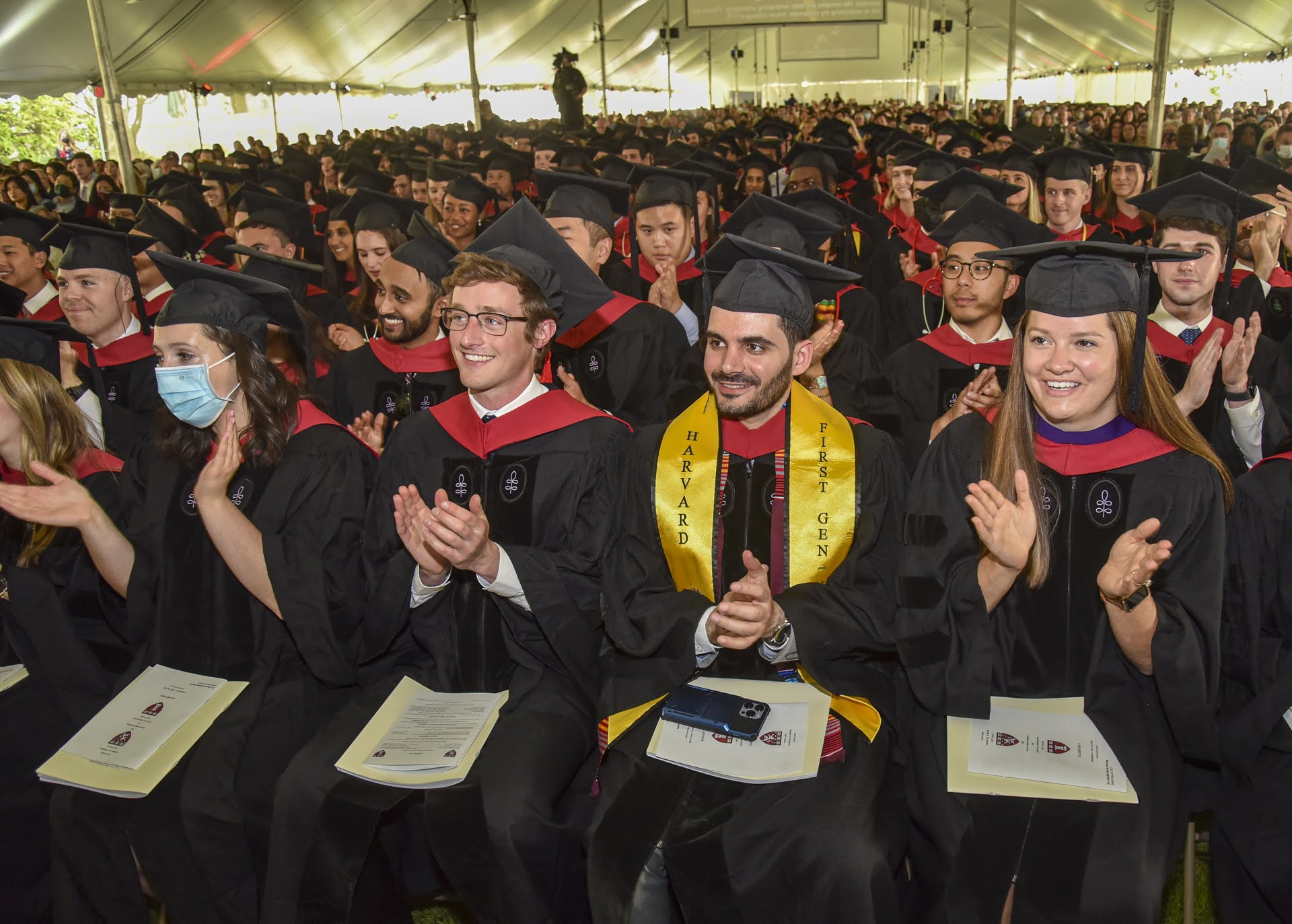 Students sitting in audience, wearing regalia, clapping