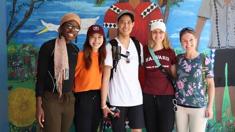 Students casually dressed stand in front of a brightly painted mural.