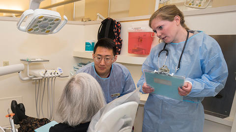 Two clinicians talking to a patient sitting in a dental chair.