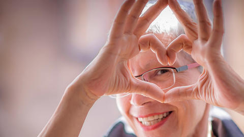 Cute senior old woman making a heart shape with her hands and fingers