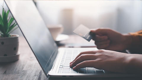 close up of a laptop with one hand on the keys and another holding a credit card