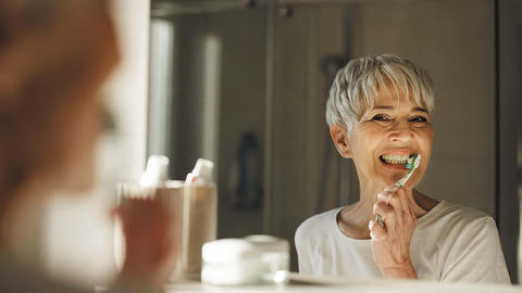 older woman looking in the mirror and brushing her teeth