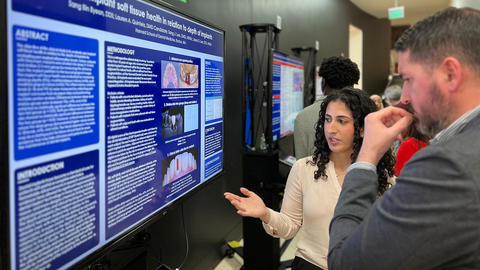 student pointing to screen describing her research to a judge