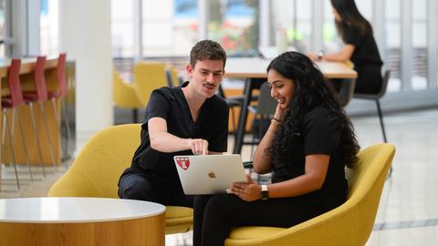 two students in the REB lobby looking at laptop
