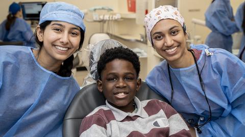 two students in PPE with flank a child sitting in dental chair