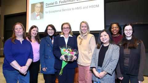 Sara holding a silver bowl and flowers surrounded by her colleagues