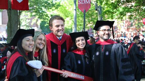 smiling grads in cap and gown holding the HSDM tooth brush