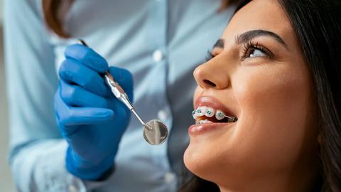 close up of a patient with braces with an examination mirror in front of her mouth