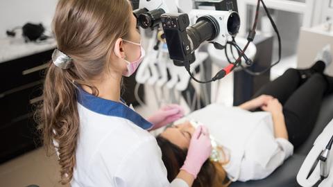 Female dentist with dental tools - microscope, mirror and probe checking up patient teeth at dental clinic office. Medicine, dentistry and health care