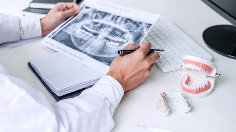 Dentist writing report working with tooth x-ray film, model and equipment used in the treatment of dental and dentistry at workplace