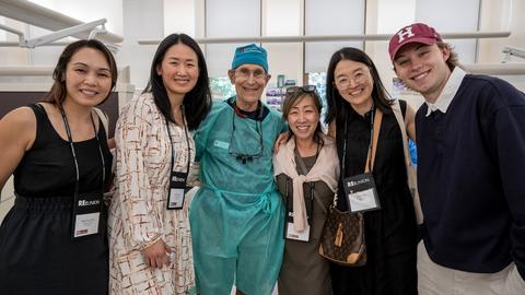 Six HSDM community members gather in a dental teaching clinic during Reunion, including a faculty member wearing surgical attire.