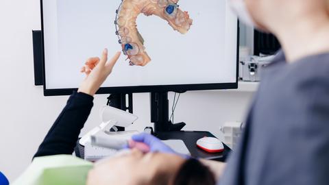 Dentist discussing digital dental 3D scan mold with female patient with braces in dental office
