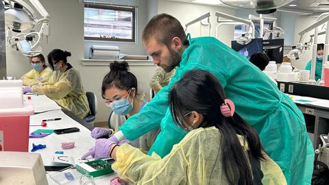 Pre-dental participant practices with dental instruments while an instructor observes in a dental teaching clinic.