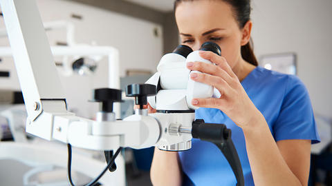 woman in blue scrubs looks into dental microscope