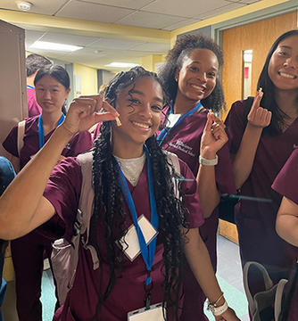 Smiling students in scrubs proudly display dental models.