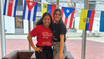 Two people standing together in front of Cuban flag