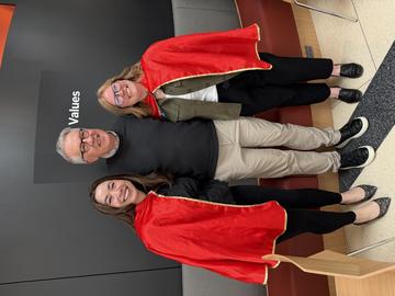 The dean with Sophie and Kathleen, who are wearing red capes