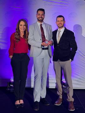 student with two professors holding an award