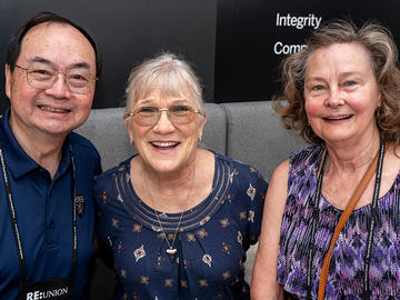 Three attendees smiling together at a symposium reception.