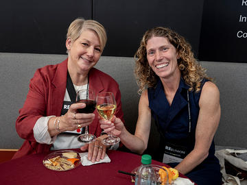Two attendees seated together sharing a toast at a Alumni Day reception.