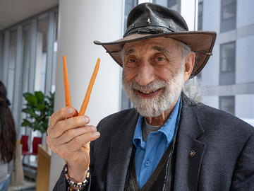 An attendee wearing a hat smiles while holding two carrots in the shape of the letter V.