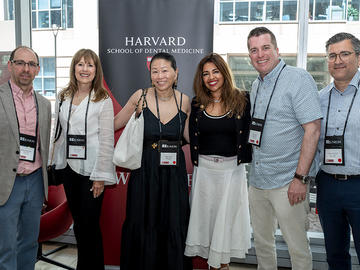 Six attendees pose together in front of a Harvard School of Dental Medicine pop-up banner..