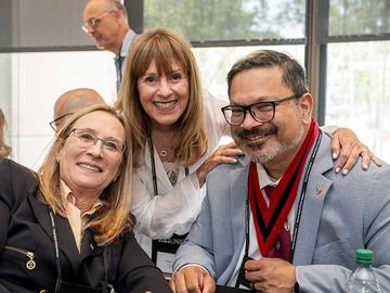 Three alumni smiling together while seated at a table.