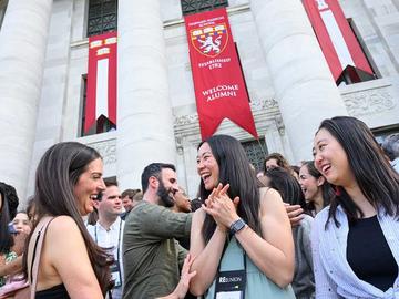 Alumni talking outside of Harvard Medical School's Gordon Hall building with school banners displayed overhead.
