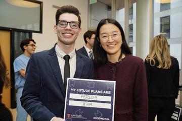 A student standing with a faculty member holding a blue sign