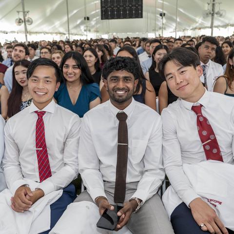 Four students sitting together under a white tent