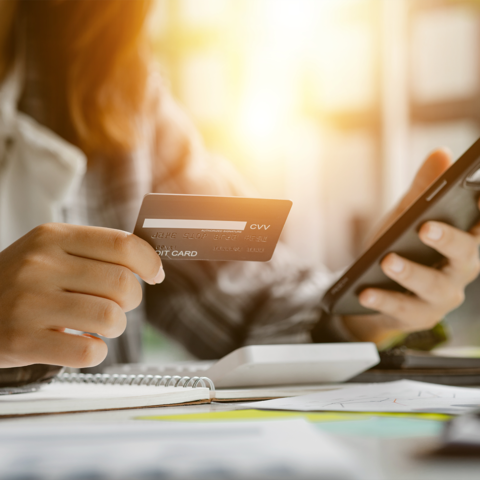 cropped image showing a one hand holding an credit card and the other holding a mobile phone