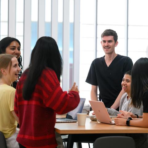 Students gather and talk around a table in a campus common area.