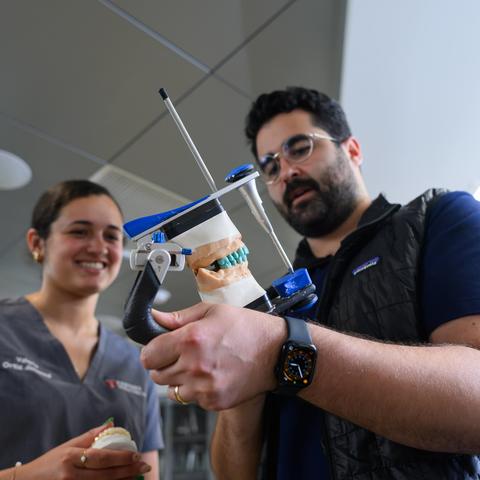 instructor holding a model of teeth next to a student