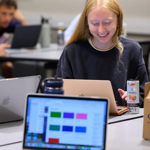 two students smiling and sitting in front of open laptops