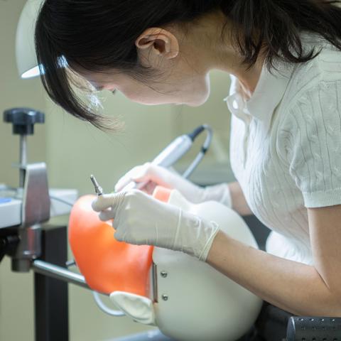 student bending over a model using dental instruments.