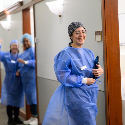 Student in PPE entering an exam room with clinicians also in PPE in background