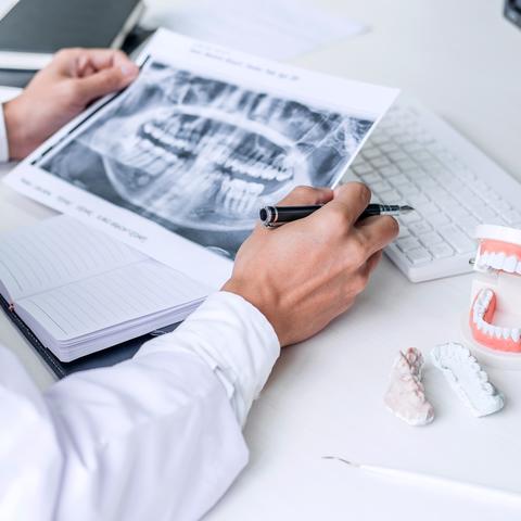 Dentist writing report working with tooth x-ray film, model and equipment used in the treatment of dental and dentistry at workplace