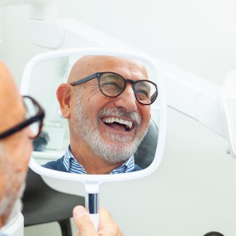 Senior man admiring his new smile in dental clinic mirror