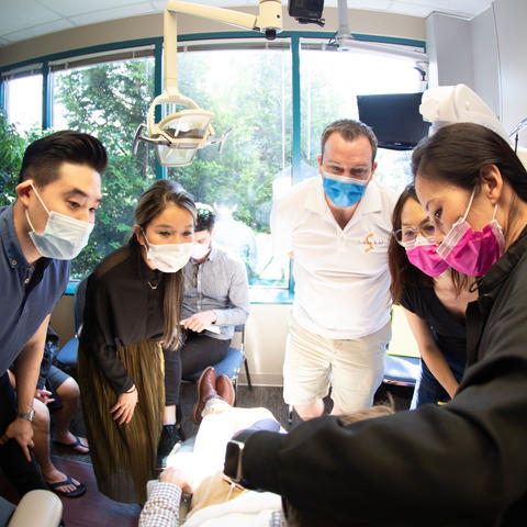 Clinicians with masks surrounding a patient in a chair