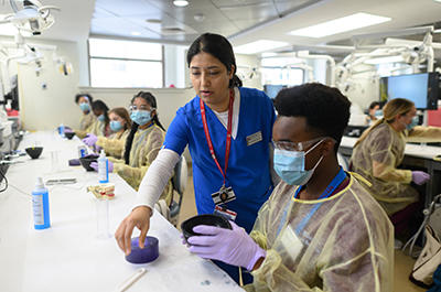 Students in masks and gowns learn dental techniques in a hands-on workshop at HSDM.