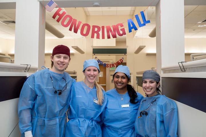 students in the clinic standing under a banner that says Honoring All
