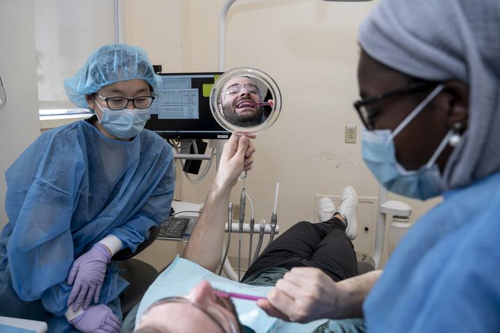 students in PPE with a patient holding a mirror and smiling