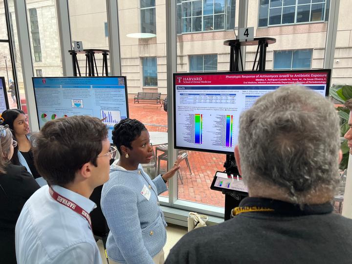 Student in front of a monitor displaying her research and explaining it to two faculty members