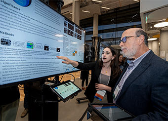 Student in front of a poster explaining results to a symposium participant.