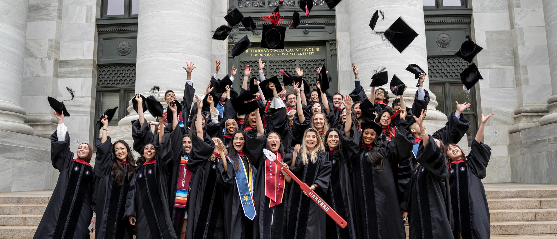 Grads throw up caps in the air on the steps of Gordon Hall