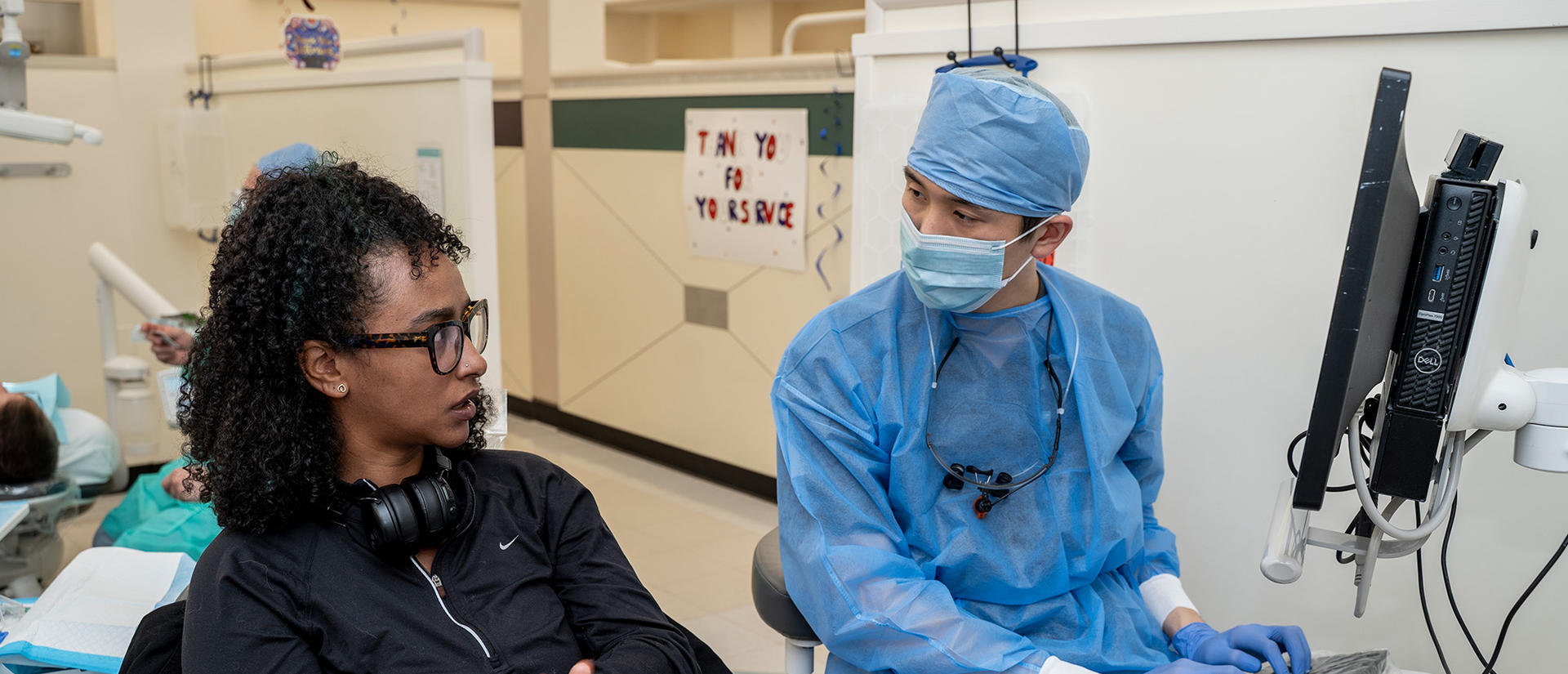patient in a dental chair talking with a student in full PPE