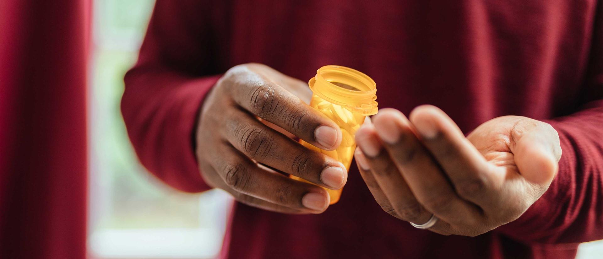 cropped image of a person holding a presciption vial with pills and the other hand is opened