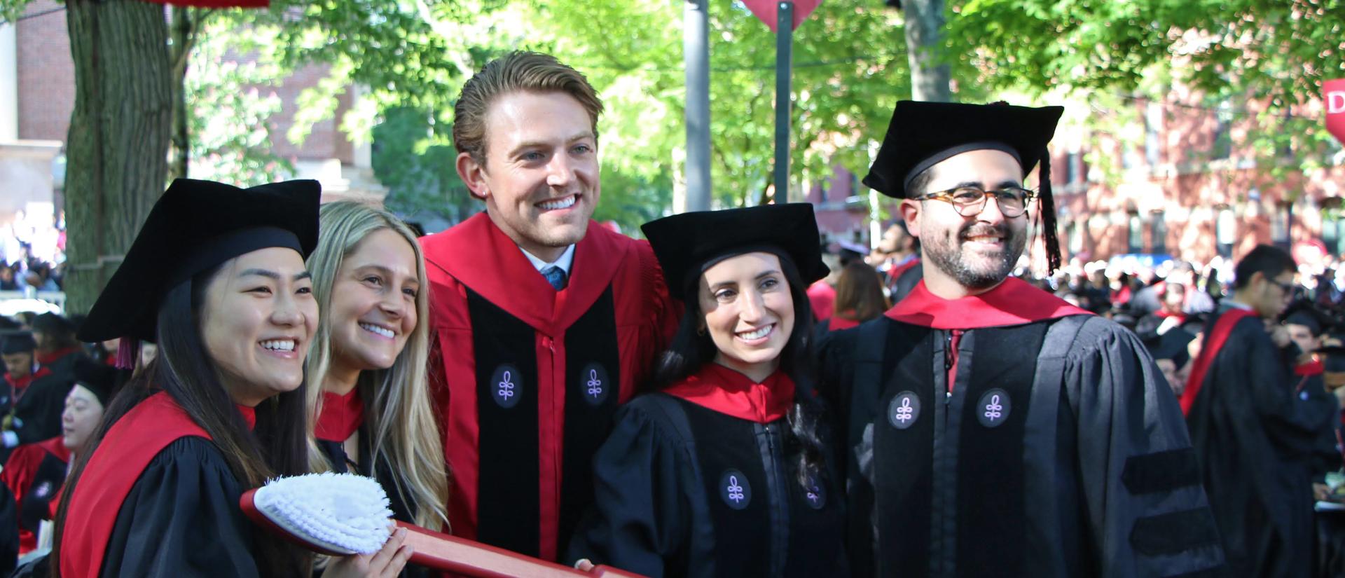smiling grads in cap and gown holding the HSDM tooth brush