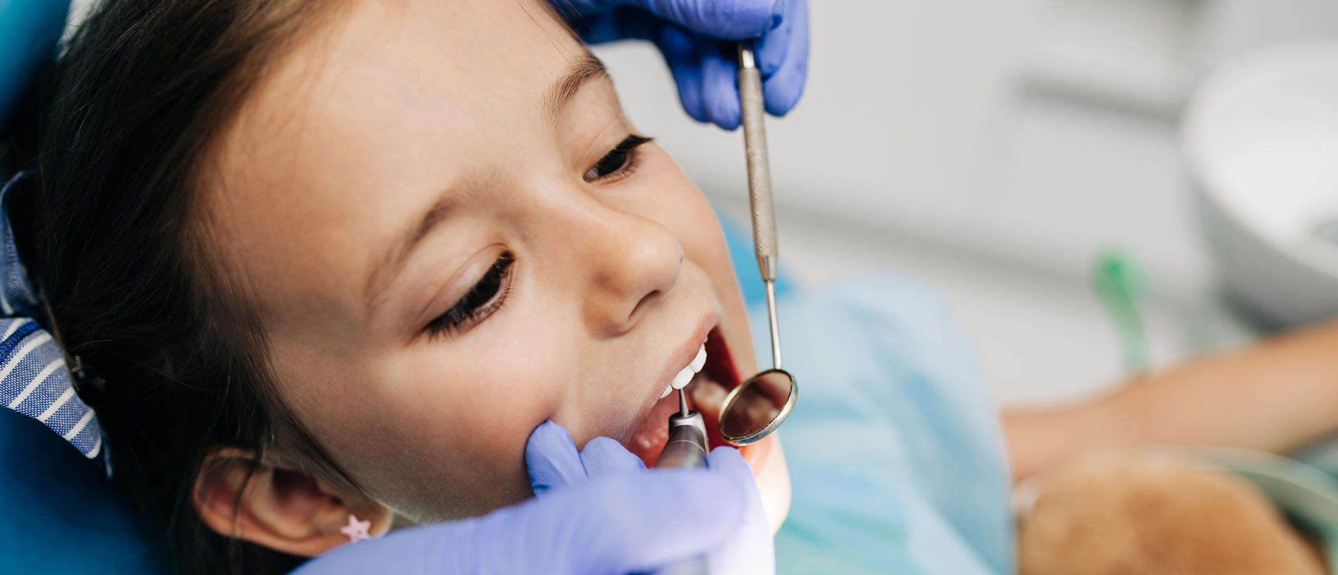 Young child receiving a dental examination from a dentist using dental tools in a pediatric dental office.